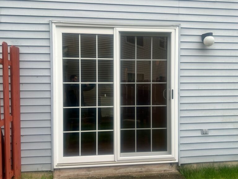 Exterior view of a closed white sliding glass door on a house with light blue siding